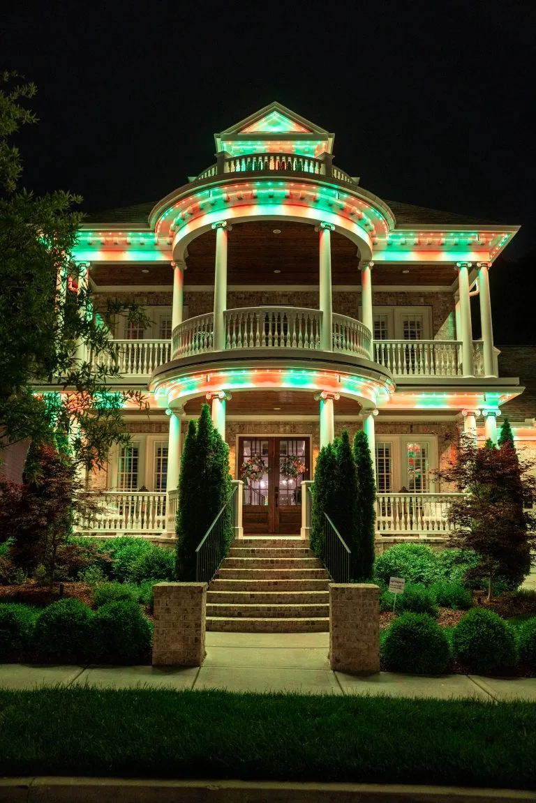 A beautifully lit historic house is adorned with colorful holiday lights at night
