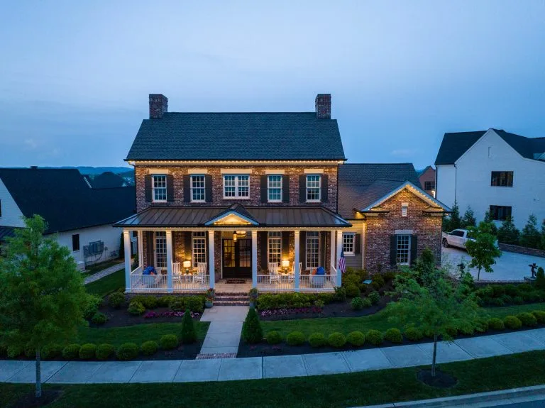 A charming two-story house is illuminated as dusk settles, with landscaped gardens