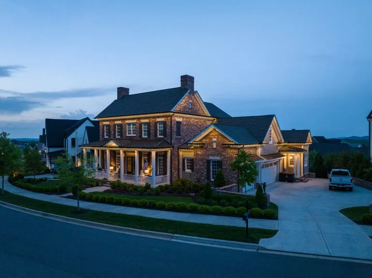 A beautifully illuminated house stands at dusk, showcasing its charming architecture and landscaped yard