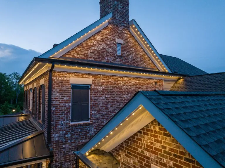 Warm lights illuminate the brick exterior of a charming home at dusk