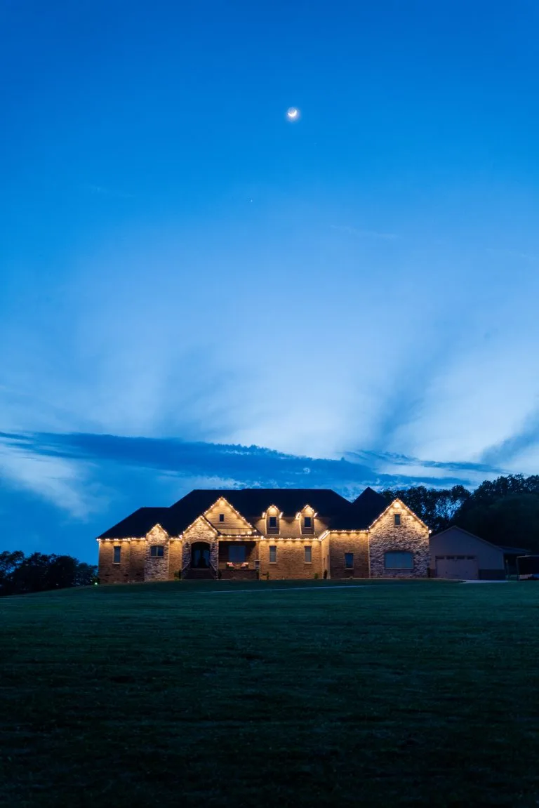 A beautifully lit house stands under a twilight sky with wispy clouds