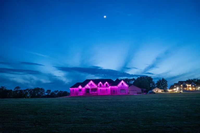 A large house is illuminated in pink lights under a twilight sky