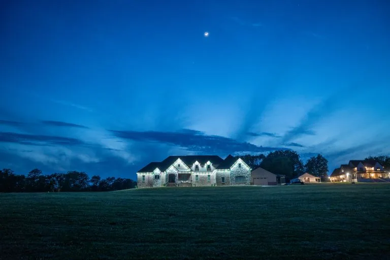 A beautifully lit house stands against a twilight sky with scattered clouds