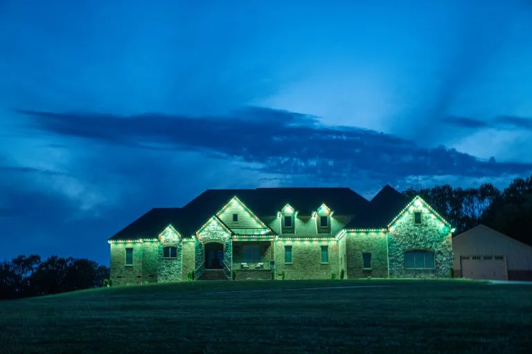 A large house is illuminated with green lights against a twilight sky