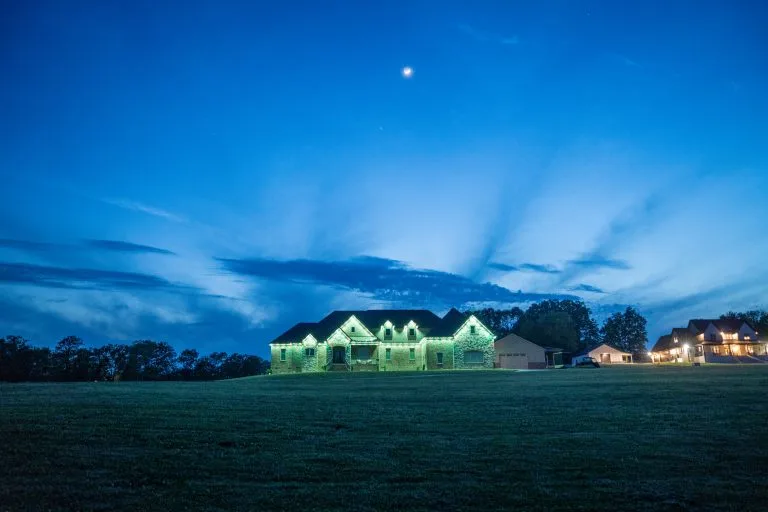 A softly lit house glows green against a twilight sky with scattered clouds