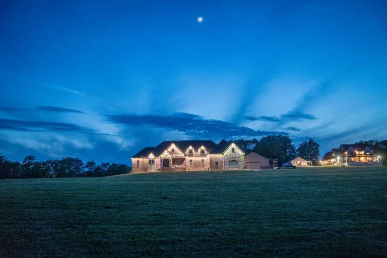 A large, illuminated house stands against a twilight sky with wispy clouds