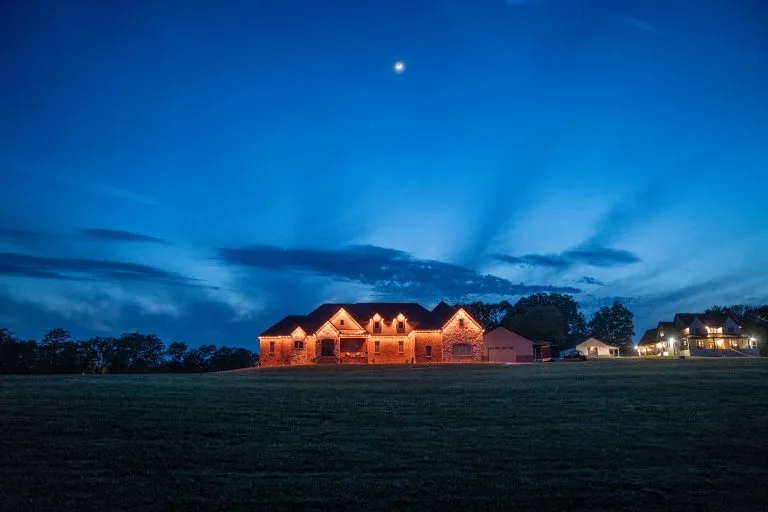 A beautifully illuminated house glows against a twilight sky with scattered clouds