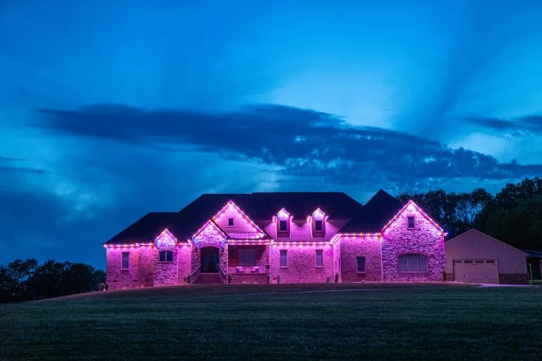A beautifully lit stone house glows with vibrant pink lights against a twilight sky