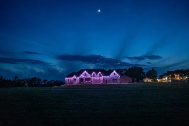 A large house illuminated with pink lights stands against a twilight sky
