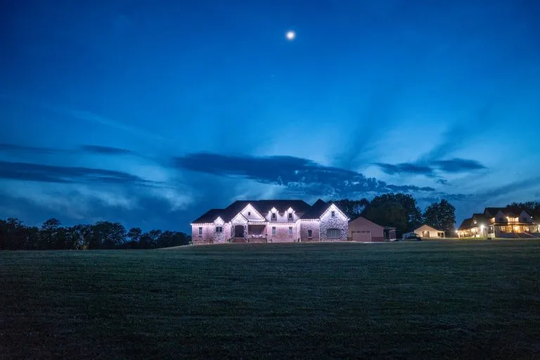A large, illuminated house stands against a twilight sky with scattered clouds