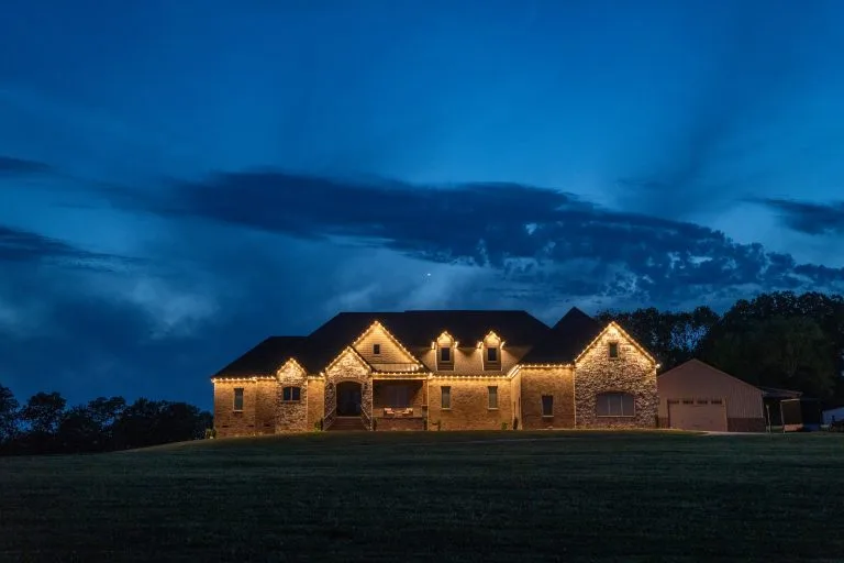 A beautifully lit stone house stands under a twilight sky with dramatic clouds