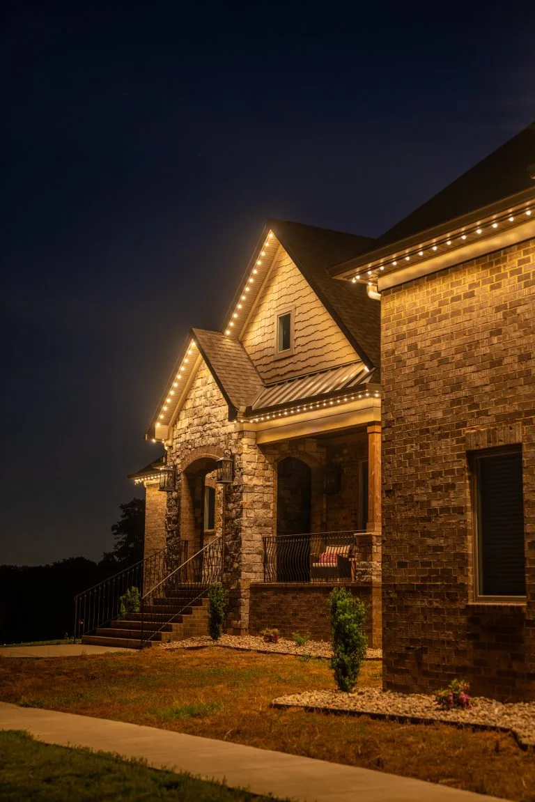 Warm lights outline a charming brick house against a dark evening sky