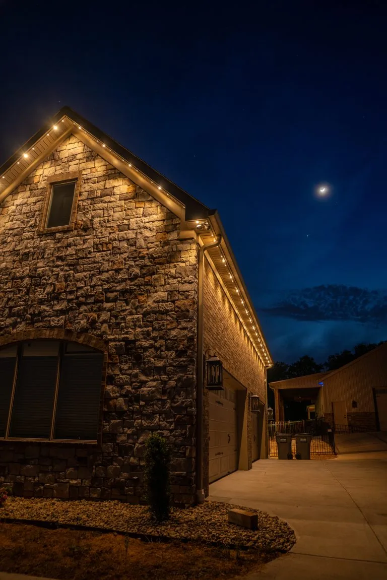 A stone house is illuminated by warm lights under a twilight sky