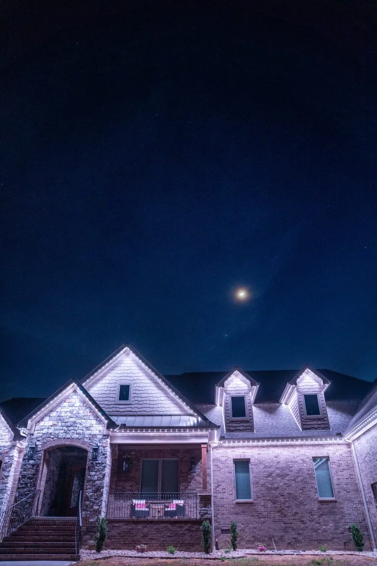 A beautifully lit house stands under a dark night sky with a crescent moon