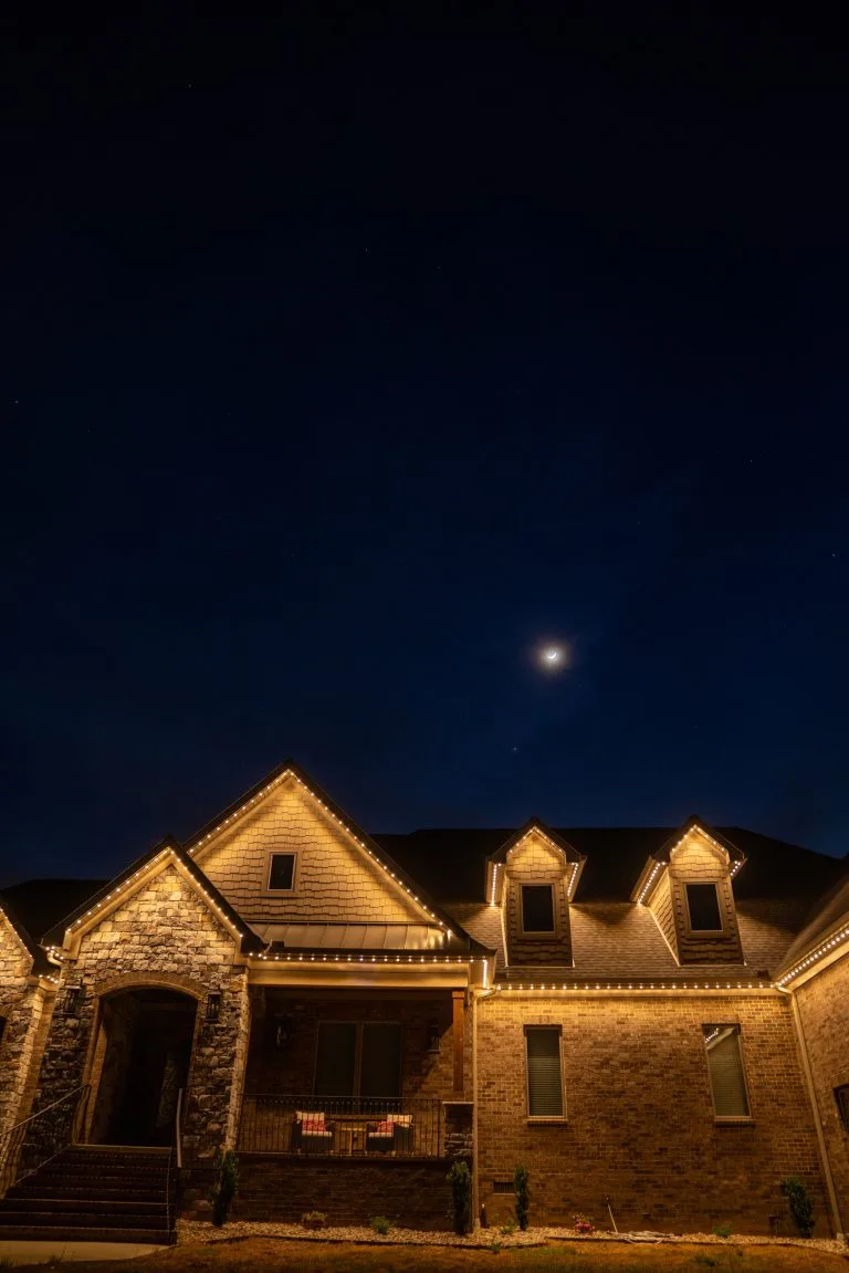 A beautifully lit house stands beneath a crescent moon in the night sky