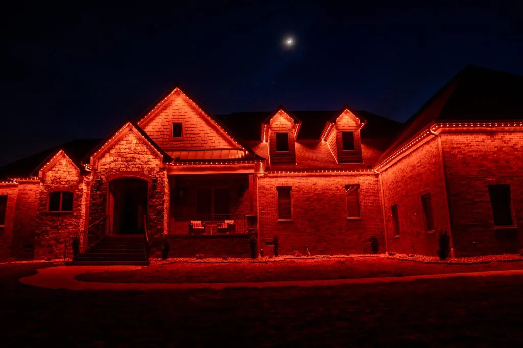 Gemstone lights installation illuminates a brick house with vibrant orange hues at night
