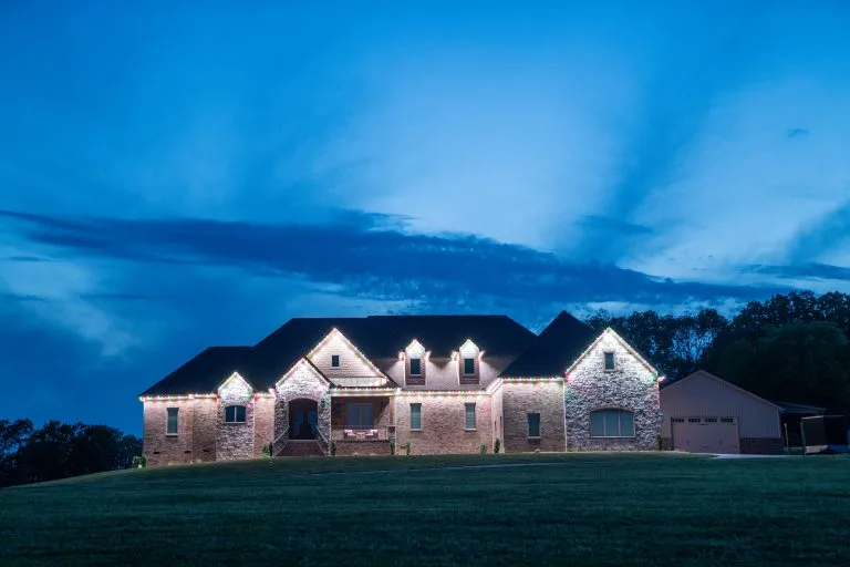A beautifully lit house glows against a twilight sky with scattered clouds
