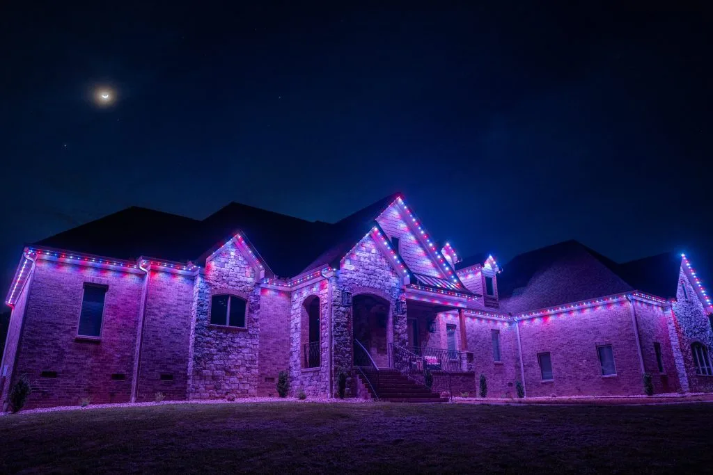 Permanent outdoor lighting illuminates a house with colorful lights against a starry night sky