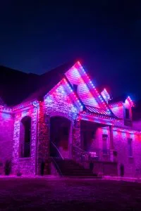 A beautifully lit house showcases vibrant purple and pink lights against a dark sky