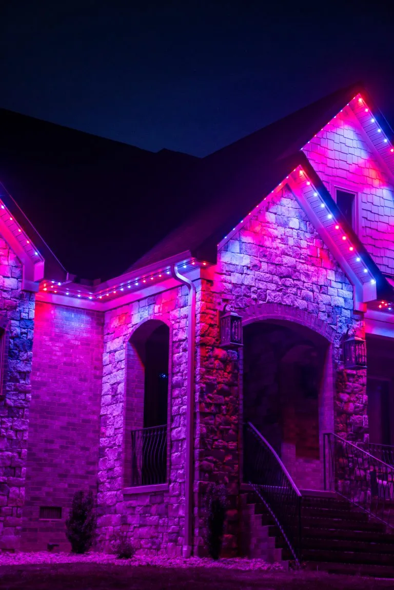 Bright purple and pink lights illuminate a stone house at night