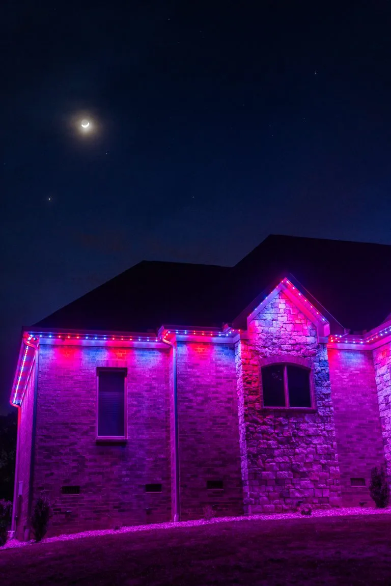A house is illuminated with vibrant pink lights against a nighttime sky