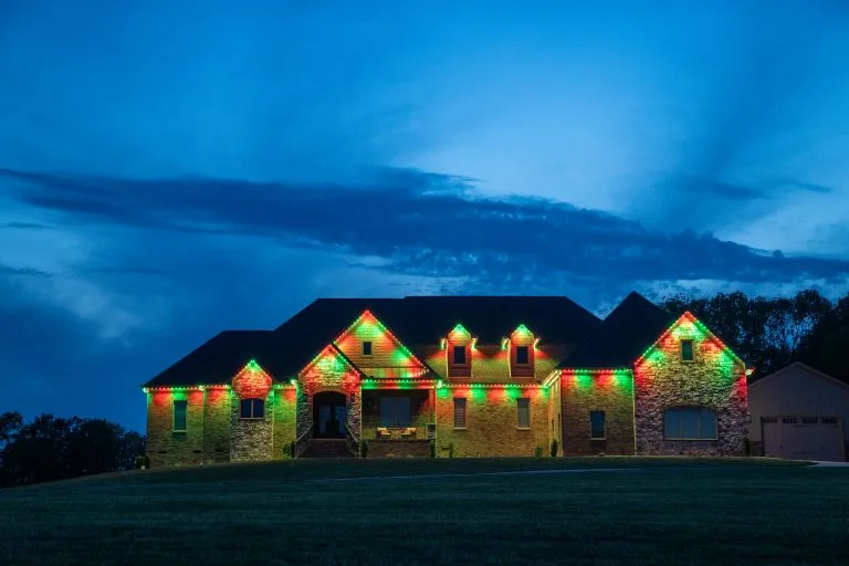 A house is adorned with colorful red and green lights against a twilight sky