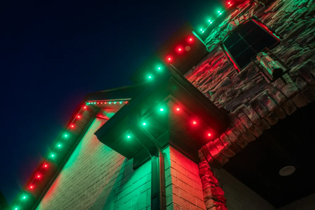 Roofline lighting in red and green illuminates house eaves against a twilight sky