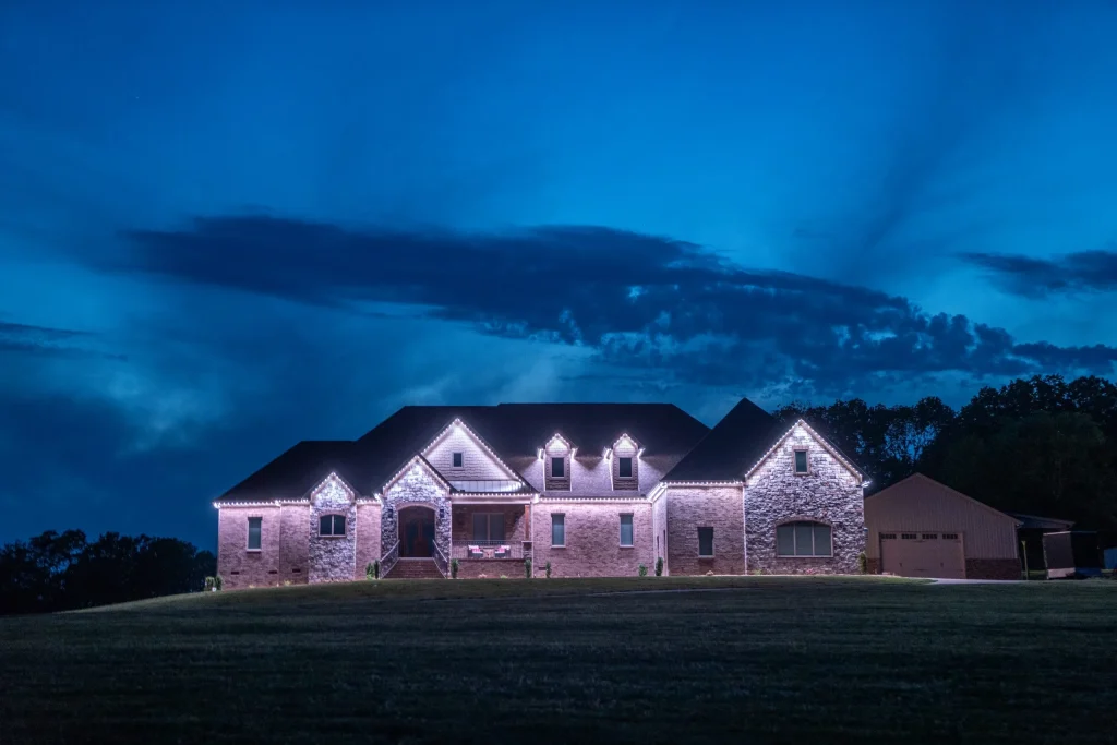 A large, illuminated stone house stands against a twilight sky filled with clouds