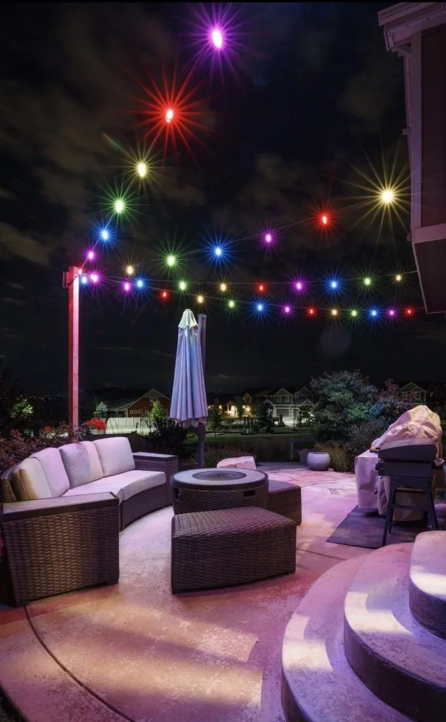 A cozy outdoor seating area is illuminated by colorful string lights against a night sky
