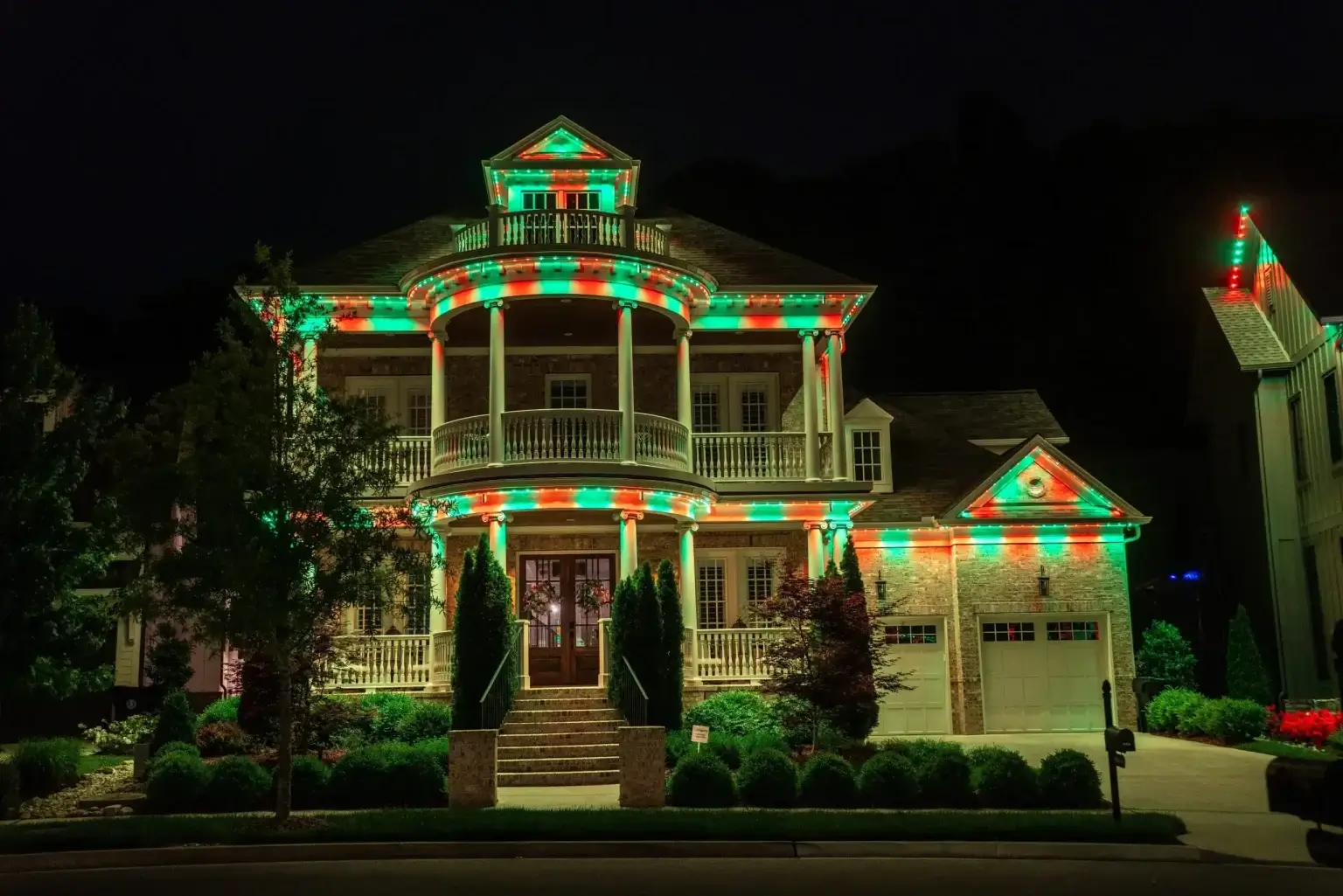 A grand house adorned with vibrant red and green holiday lights at night