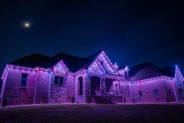 A beautifully lit house is adorned with vibrant purple and white lights at night